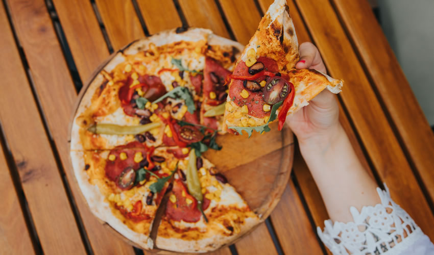overhead view of hand holding slice of vegetable pizza
