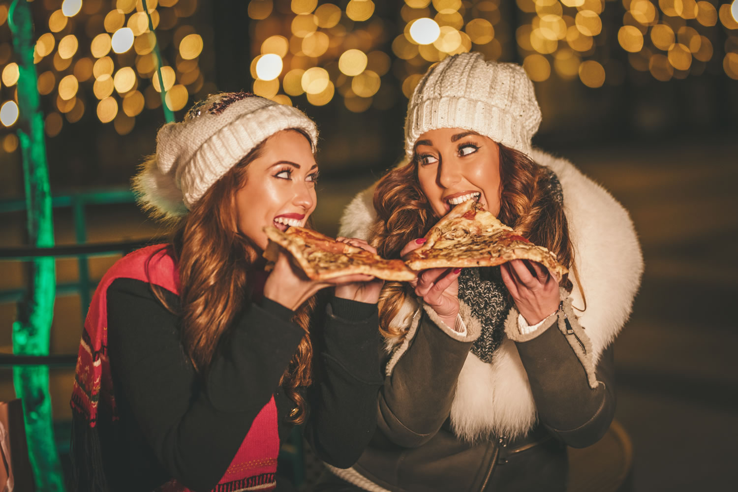 xmaspic-1 Cheerful young female friends are eating slices of pizza and having fun on a holiday winter night